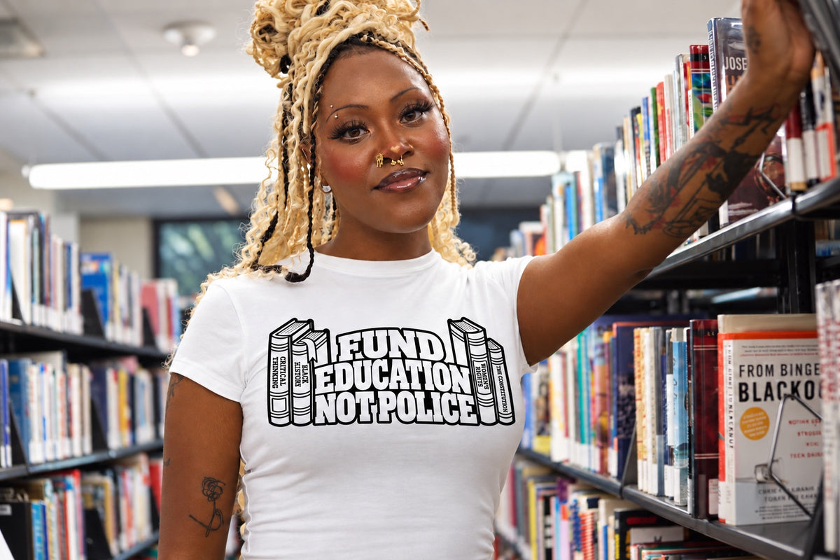 Model wearing white Fund Education Not Police Poligear tee standing in a library