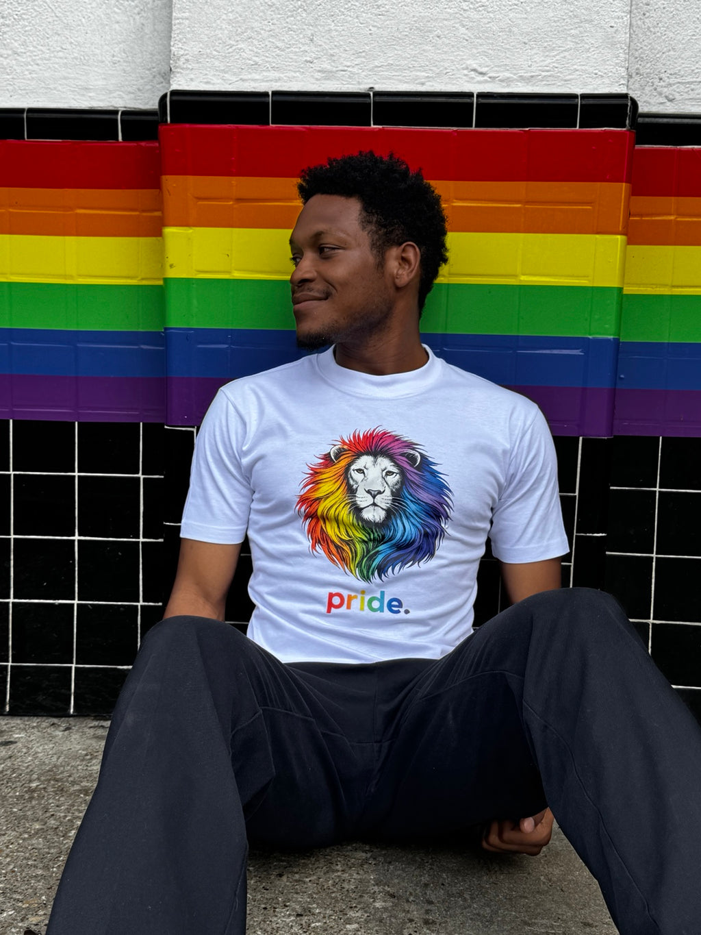 Model showing Poligear Pride lion graphic tee against a rainbow-painted wall